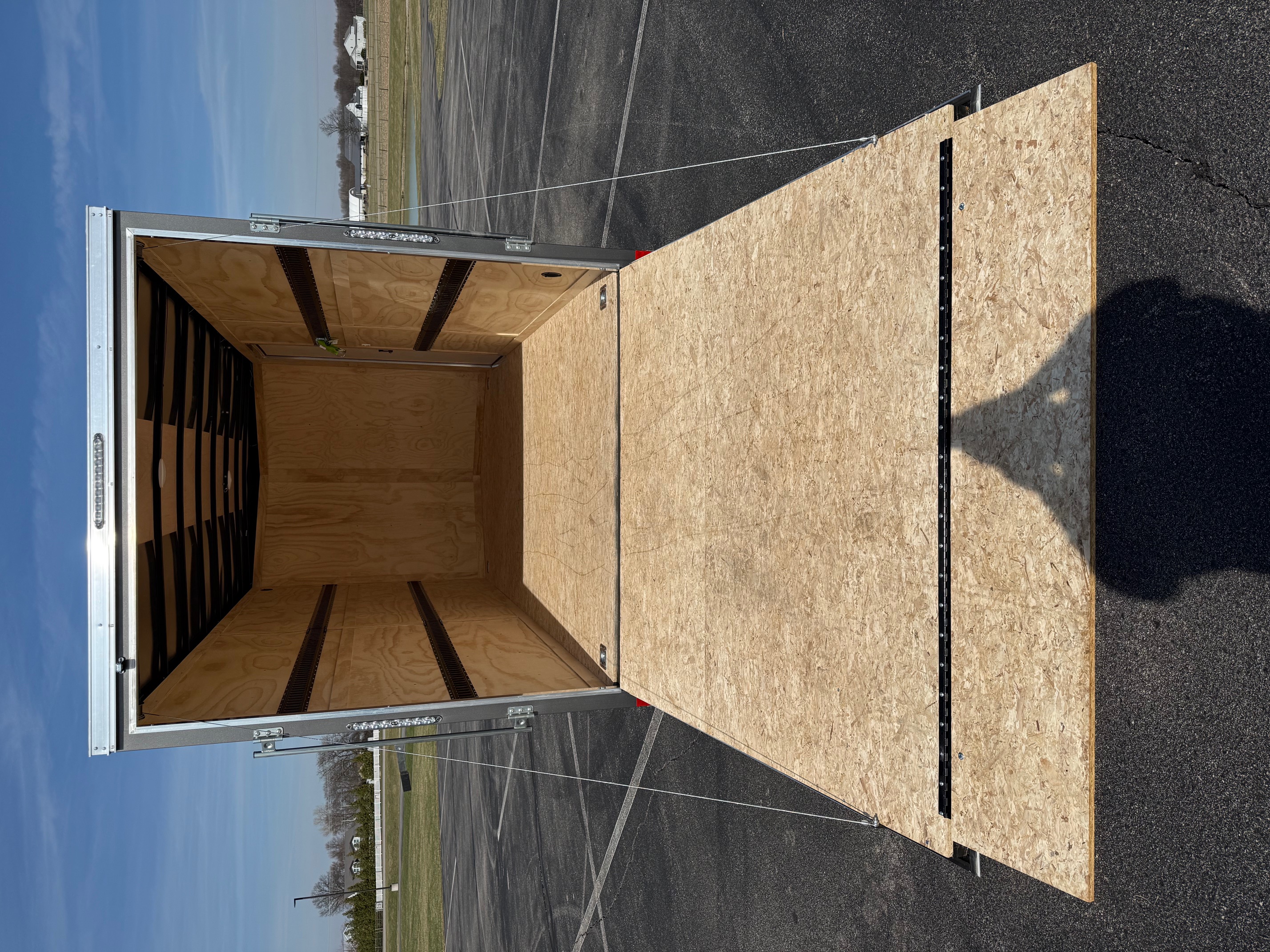 Inside view of SMS Trailer Rentals enclosed cargo trailer showing rear ramp door, plywood floor and walls in Grabill IN